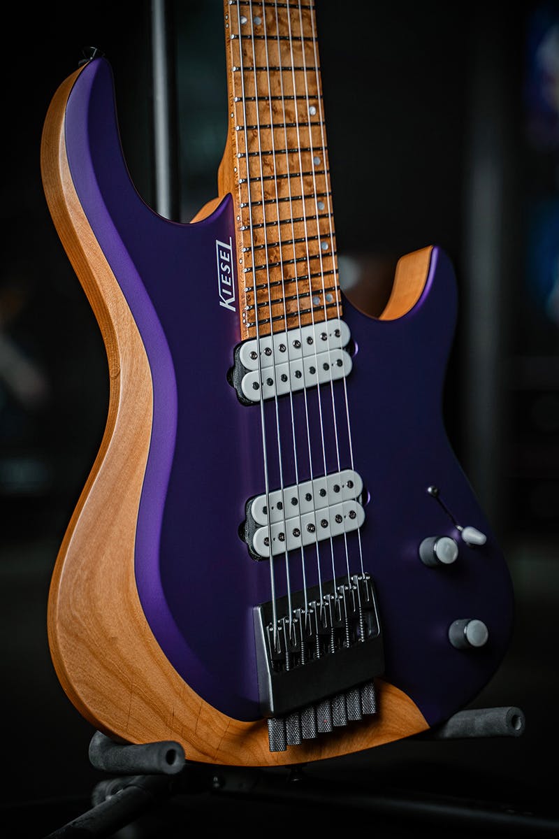 Kiesel Guitars Osiris multiscale OM7 with alder body, metallic grape jelly finish, ash top, rear natural clear back and sides RNC, roasted birdseye maple fingerboard, mother of pearl staggered offset dot inlays, white pickup coils, black hardware, white pearl knob inlays